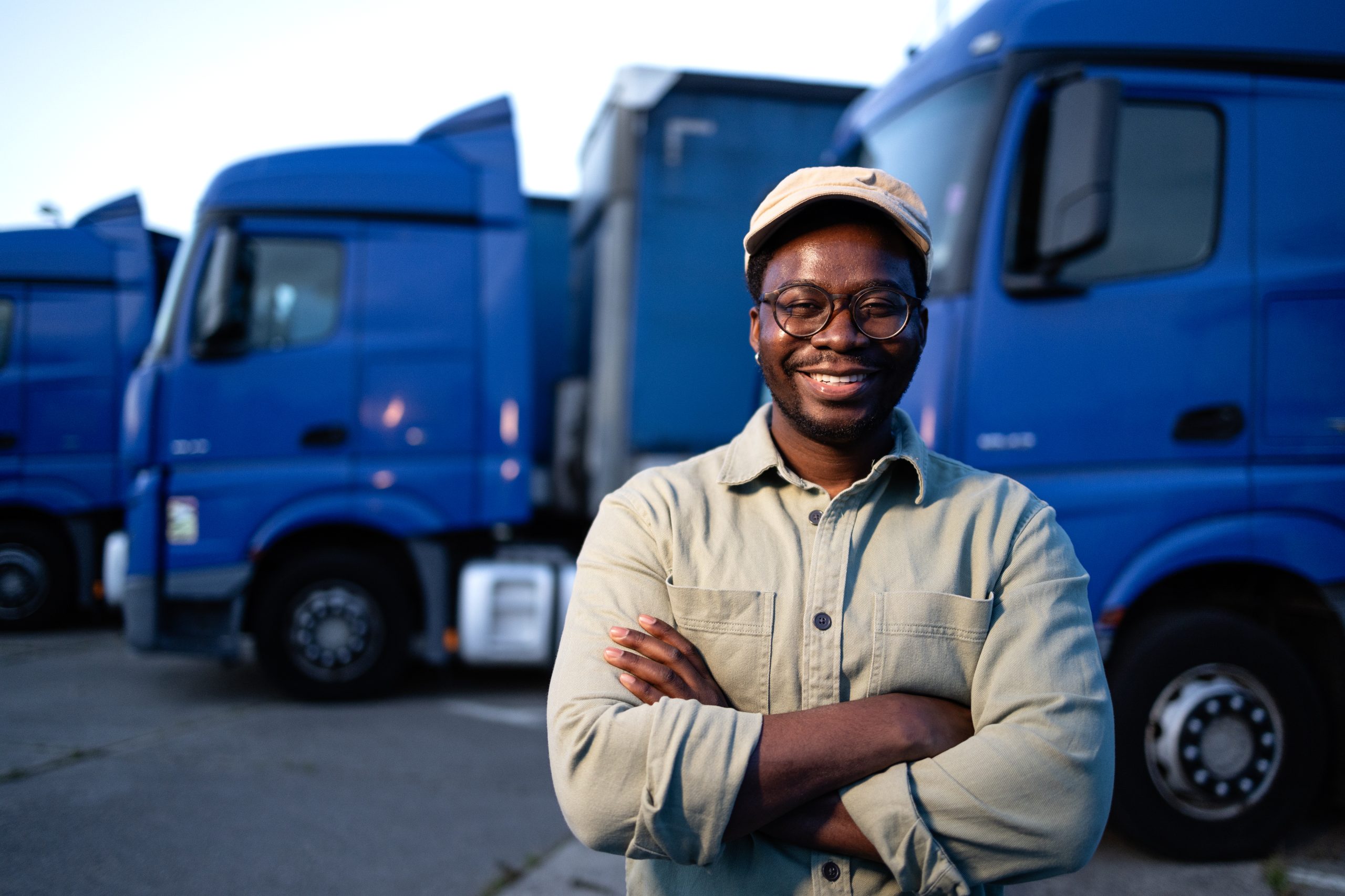 portrait of smiling driver standing in front of his trucks at parking lot.